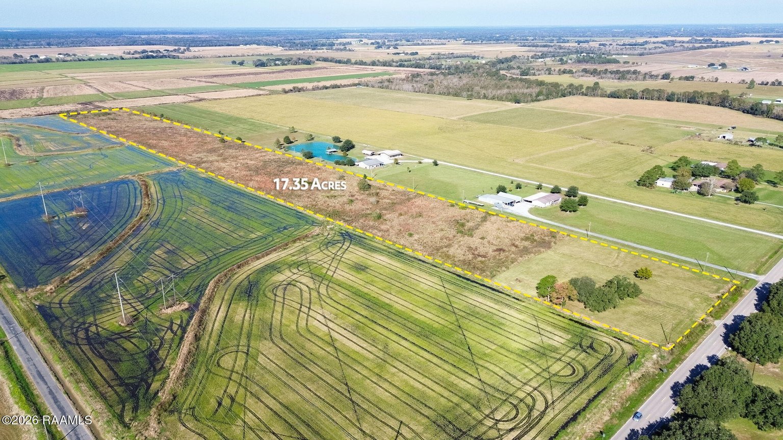 Aerial view of 17.35-acre rural property with patterned crop fields, white farm buildings, gravel driveway, scattered mature trees, and cultivated pastureland bordered by tree lines.