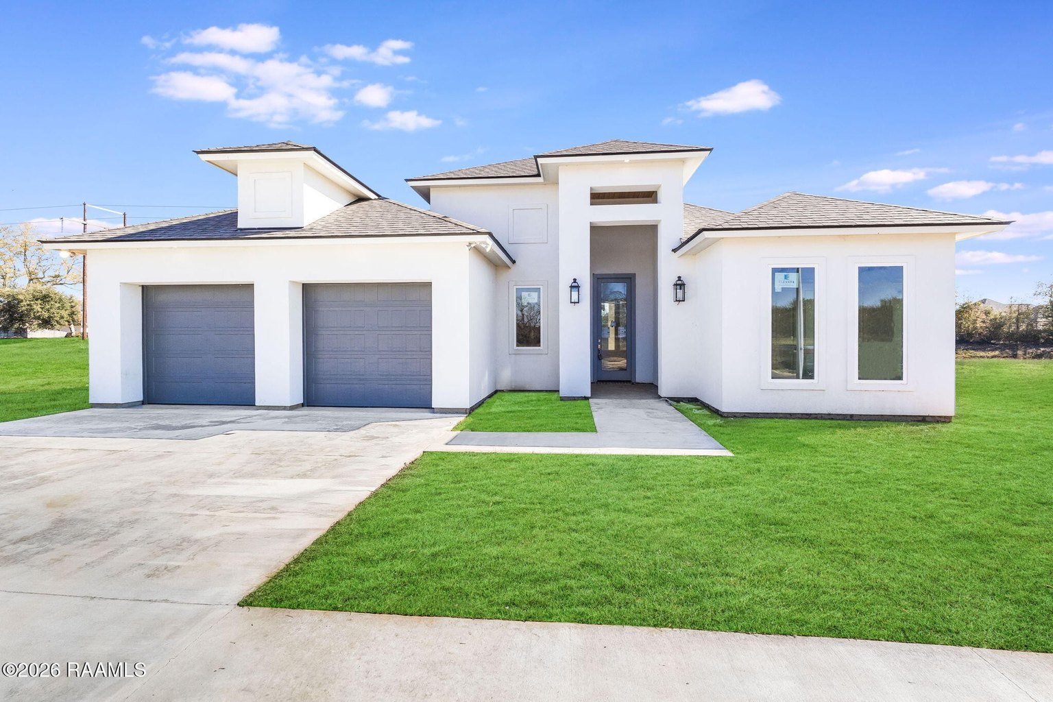 Modern white two-story home with two-car blue garage doors, gray tile roof, landscaped front lawn, concrete driveway, and clear blue sky. Geometric architecture with white stucco exterior.